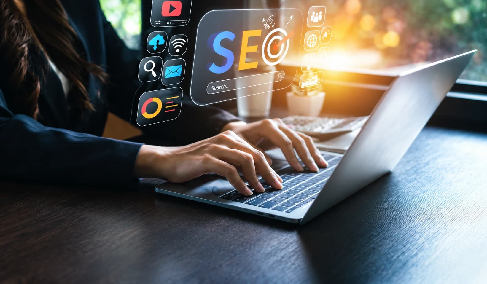 Hands typing on a laptop with search, SEO and marketing icons floating above the keyboard